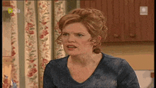 a woman in a blue shirt is making a funny face in front of a floral curtain