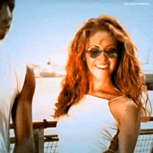a woman wearing sunglasses and a white tank top smiles for the camera