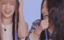 two young women are laughing and drinking from straws while sitting next to each other .