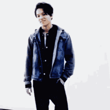 a man in a denim jacket with a hood is standing with his arms crossed and smiling .