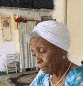 an elderly woman wearing a white turban and pearls looks down