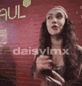 a woman is standing in front of a red brick wall with the word daisylmx written on it .