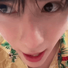 a close up of a person 's face wearing a yellow shirt with a floral print .