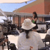 a woman in a white hat stands in front of a camera while a man holds a microphone