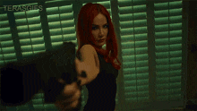 a woman with red hair is pointing a gun at the camera with the words terasgifs visible in the background