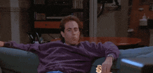 a man in a purple sweater is sitting on a blue couch
