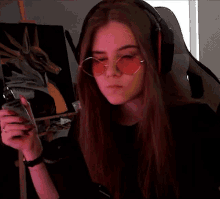 a girl wearing headphones and sunglasses is sitting in front of a painting and holding a cell phone .
