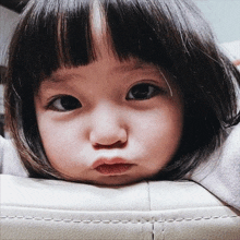 a little girl is making a funny face while laying on a white couch .