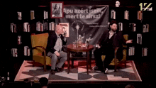 two men are sitting in front of a sign that says " apu azert iszik mert te sirsz "