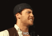 a man wearing a hat and vest is making a funny face and saying `` no '' .