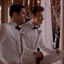 two men in white tuxedos and bow ties looking out a window