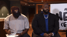 two men are sitting in front of a sign that says all