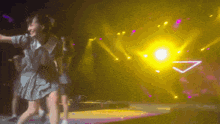 a girl in a blue dress is dancing on a stage with a yellow light behind her
