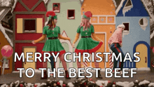 two women dressed as elves are dancing in front of gingerbread houses with the words merry christmas to the best beef