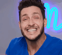 a man in a blue scrub top is smiling in front of a neon n