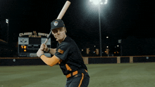 a baseball player holding a bat in front of a scoreboard that says claude smith field