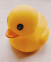 a yellow rubber duck with a black eye is sitting on a white surface .