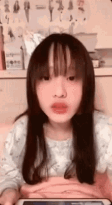 a young girl with long hair and bangs is looking at the camera while holding a tablet .