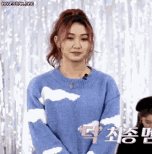 a woman wearing a blue sweater with white clouds on it is standing in front of a white curtain .