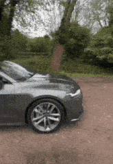 a car is parked on a dirt road in front of a tree