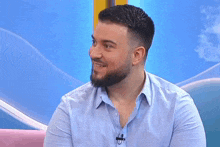a man with a beard wearing a blue shirt has a microphone on his collar