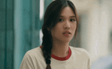 a young woman with a braided ponytail is wearing a white t-shirt with a red collar .