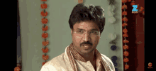 a man with glasses and a mustache is standing in front of flowers and a sign that says z on it
