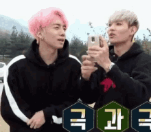 a man with pink hair is taking a selfie with another man .