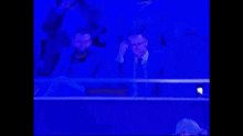 a man in a suit and tie is sitting in the stands watching a soccer game .