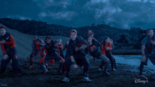 a group of people are dancing in front of a blue sky and a disney logo