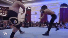 two men are wrestling in a wrestling ring while a crowd watches .