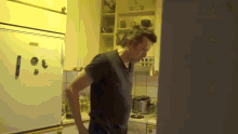 a man in a black shirt is standing in a kitchen near a refrigerator