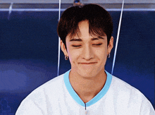 a young man wearing a white shirt with a blue collar is making a funny face with his eyes closed