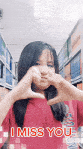 a girl in a red shirt is making a heart shape with her hands and the words i miss you on the bottom