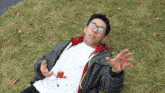 a young man is laying on the grass with blood on his shirt and glasses .