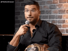 a man wearing glasses is holding a microphone in front of a brick wall with the hashtag thekomdreesen at the bottom