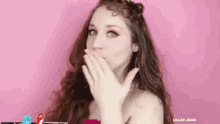 a woman with long red hair is covering her mouth with her hand .