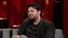 a man in a black suit is sitting on a couch with his hands outstretched