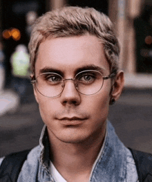 a man wearing glasses and a denim jacket is looking at the camera