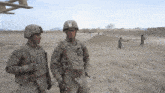 two soldiers are standing in a dirt field and one of them has the name smith on his chest