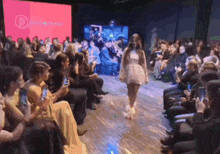 a model walks down a runway at a fashion show with a crowd watching