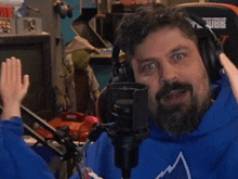 a man with a beard is wearing headphones and a blue sweatshirt with a mountain on it .