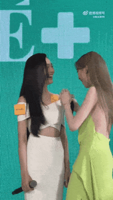 two women are standing next to each other in front of a sign that says e + on it