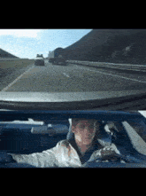 a man is driving a car on a highway with a truck behind him