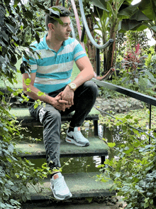 a man in a blue and white striped shirt sits on a set of stairs next to a pond