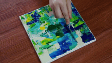 a person is painting a blue and green painting on a wooden surface