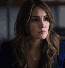 a woman wearing a blue jacket and a necklace with two circles on it