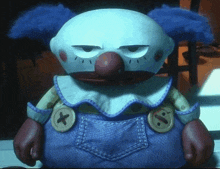 a stuffed clown with blue hair and buttons on his pants is sitting on a table in a dark room .