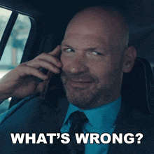 a man in a suit and tie is talking on a cell phone with the words what 's wrong behind him