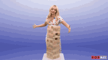a woman in a polka dot dress is standing next to a stack of wooden blocks with popbuzz written on the bottom